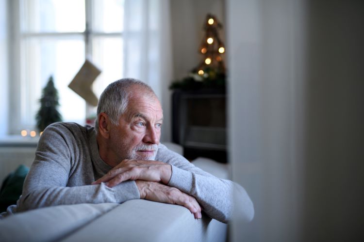 older senior man looking out window feeling sad and lonely over the holidays
